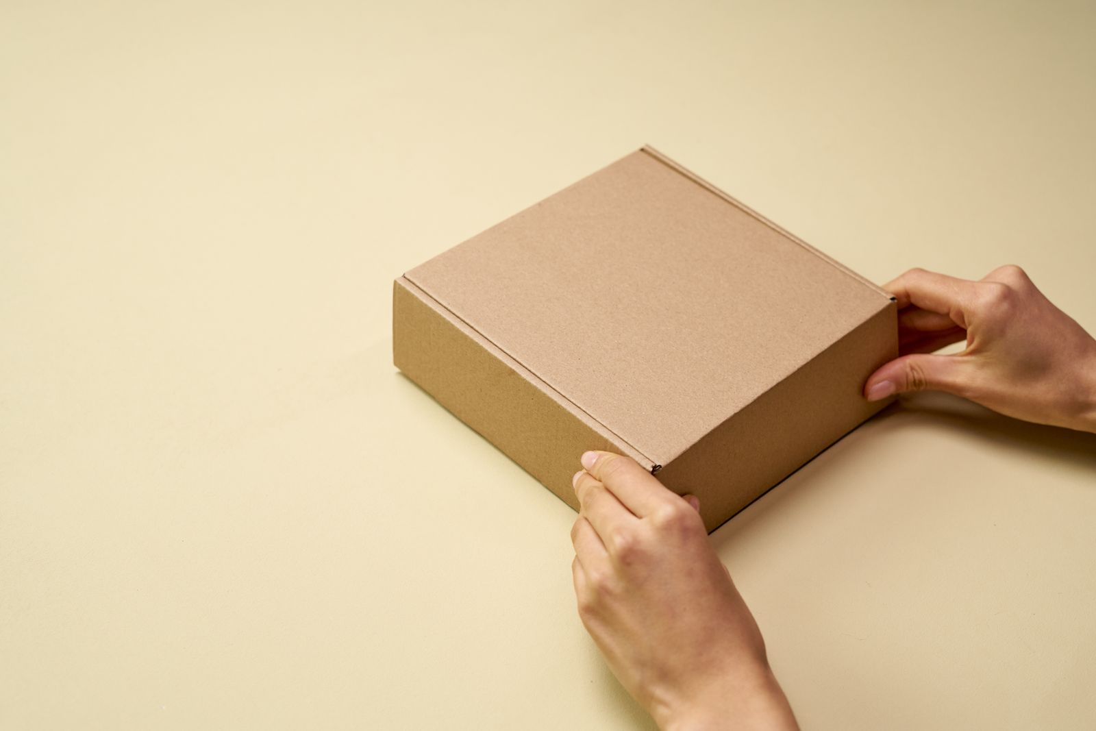 Hands opening a small cardboard parcel on a neutral surface.